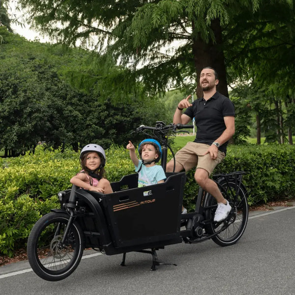 Father cycling the Aitour Basalt cargo bike with two children seated safely in the front box.