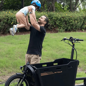 Smiling man lifting his child while standing next to the Aitour Basalt electric cargo bike.