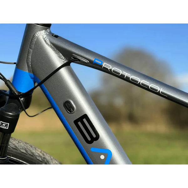 Close-up view of the Basis Protocol bike’s top tube featuring the “Protocol” logo and internal cable routing against a blue sky.