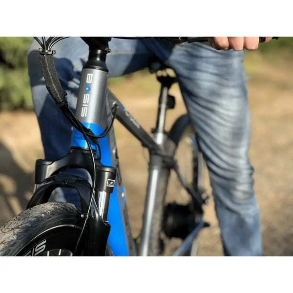 Front view of the Basis Protocol electric bike showing the suspension fork, head tube with logo, and a rider in motion.