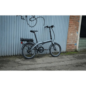 Falcon Compact Electric Folding Bike 250W parked outdoors beside a corrugated metal wall.