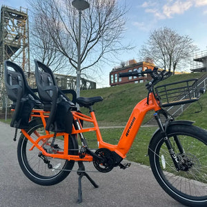 The Revom Multi C2 family electric bike with two child seats on a paved path in an urban area.