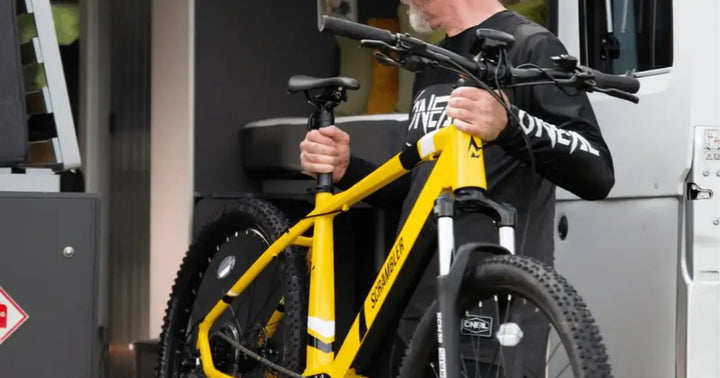 Man lifting a yellow electric mountain bike into the storage.