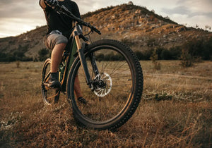 A rider on an electric mountain bike riding off-road on a grassy hill trail with rugged terrain in the background