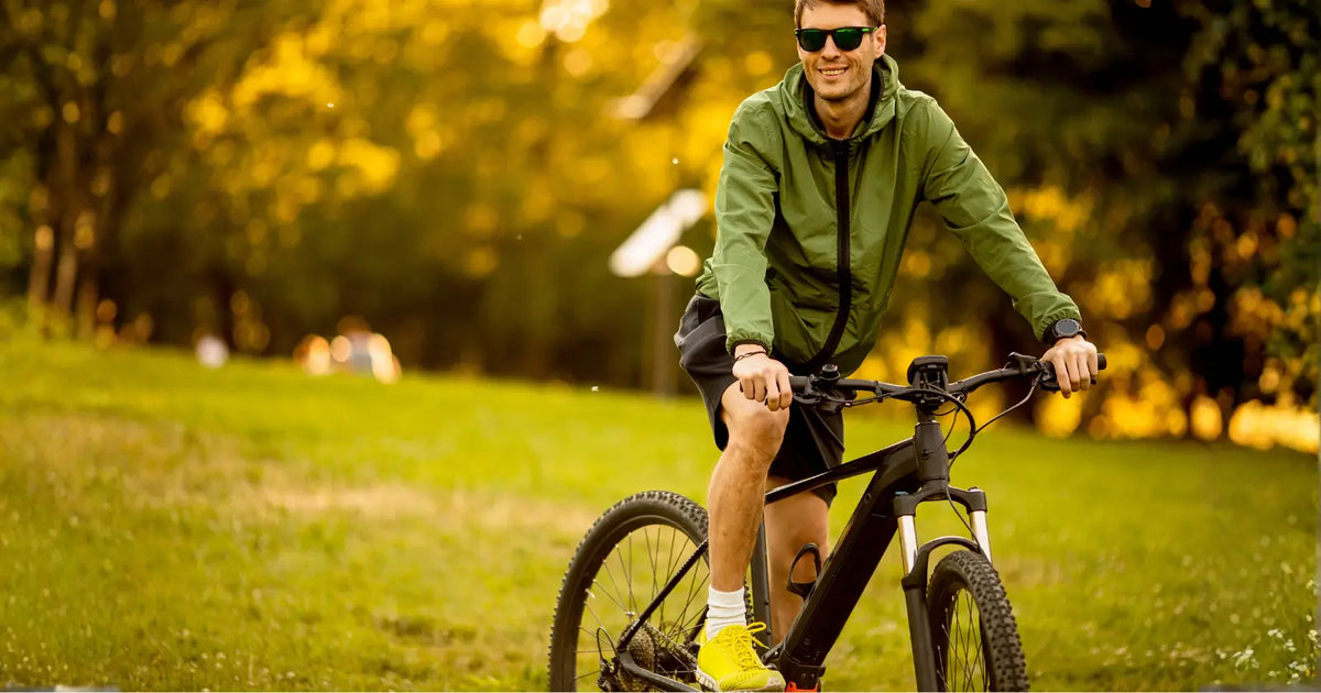 Man riding an electric mountain bike through a park during golden hour sunlight.