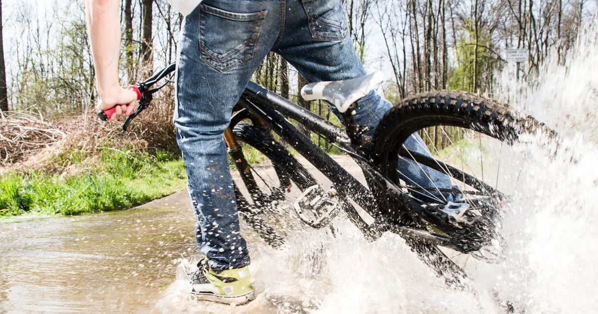 Electric bike riding through shallow water with splash, demonstrating wet weather capability.