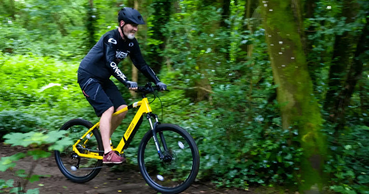 Rider cycling an electric mountain bike along a wooded forest trail.