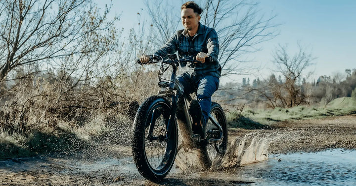 A rider powering through a muddy trail on a fat tyre electric bike, splashing water as the wide tyres grip the terrain.