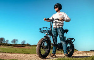 Rider standing on a fat tyre electric bike on a countryside trail under a clear blue sky.