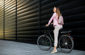 Woman commuting on an electric bike in an urban city setting with backpack and casual clothing.