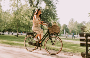Woman riding an electric bike through a park on a sunny day with a basket on the front