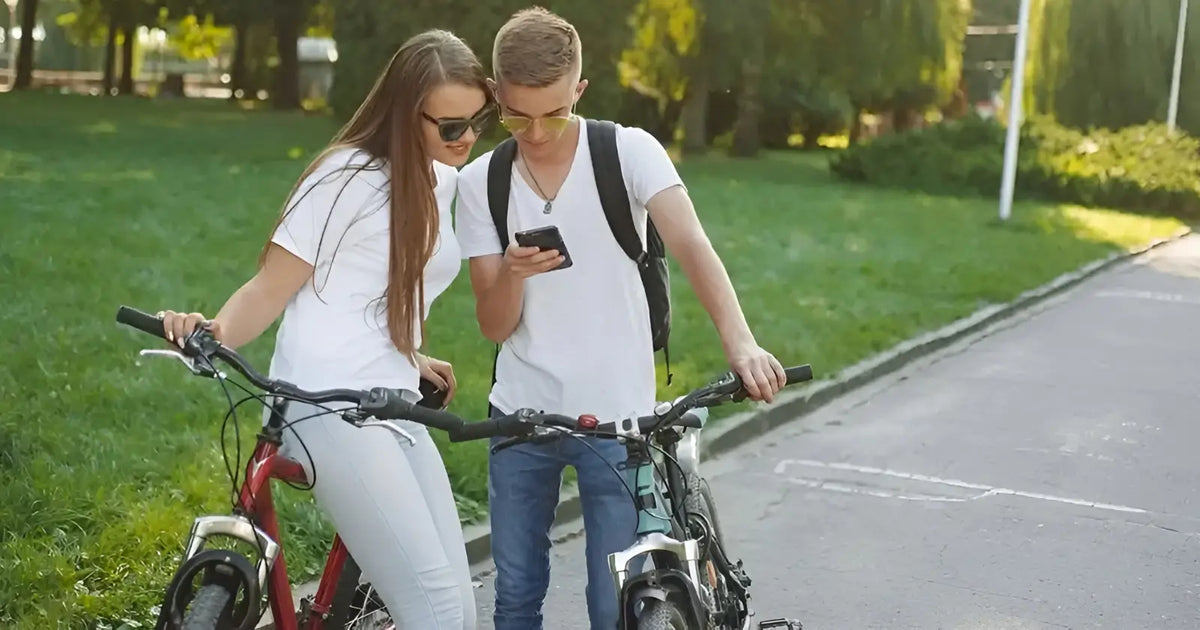 Young couple standing with electric bikes while checking a smartphone in a park.