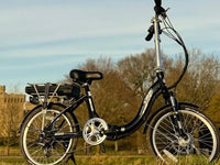 Dallingridge step-through electric bike parked outdoors in a countryside setting with a rear rack and battery mounted above the rear wheel.