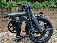 E-Go CarbonLite 3S belt drive folding electric bike folded on a gravel drive in front of a brick wall
