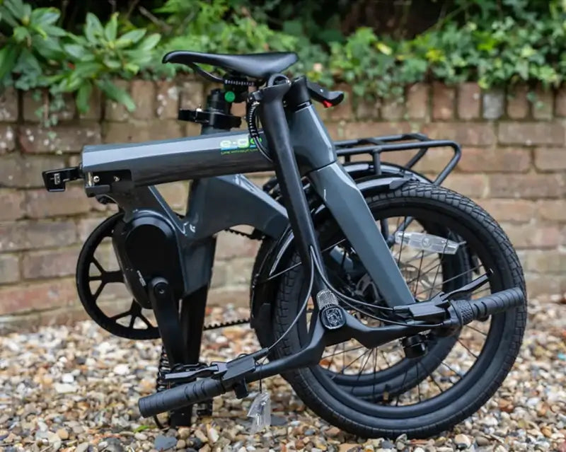 E-Go CarbonLite 3S belt drive folding electric bike folded on a gravel drive in front of a brick wall