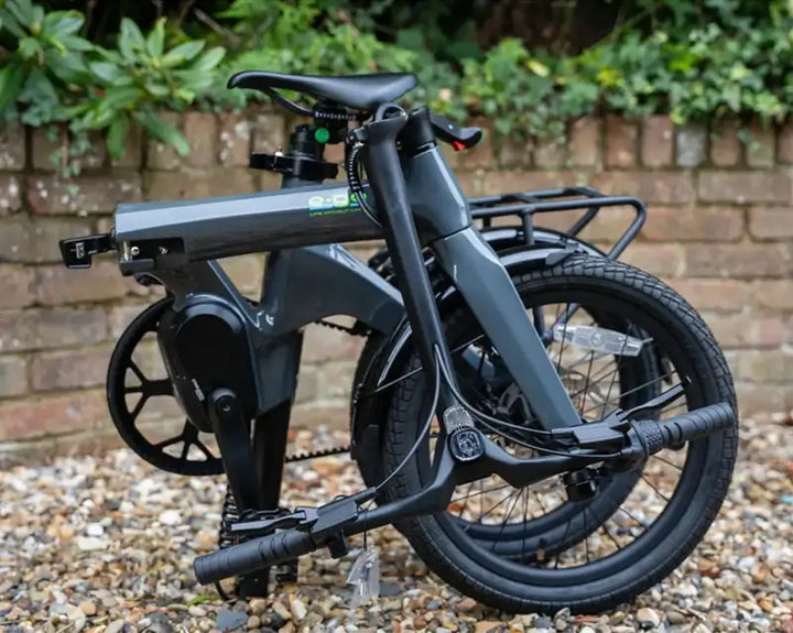 E-Go CarbonLite 3S belt drive folding electric bike folded on a gravel drive in front of a brick wall