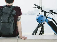 Commuter sitting beside a modern electric bike with helmet and backpack, highlighting the convenience of e-bikes for everyday urban travel.