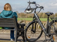 Hygge Aarhus Step-through electric bike parked beside a bench with a cyclist relaxing in a countryside setting.