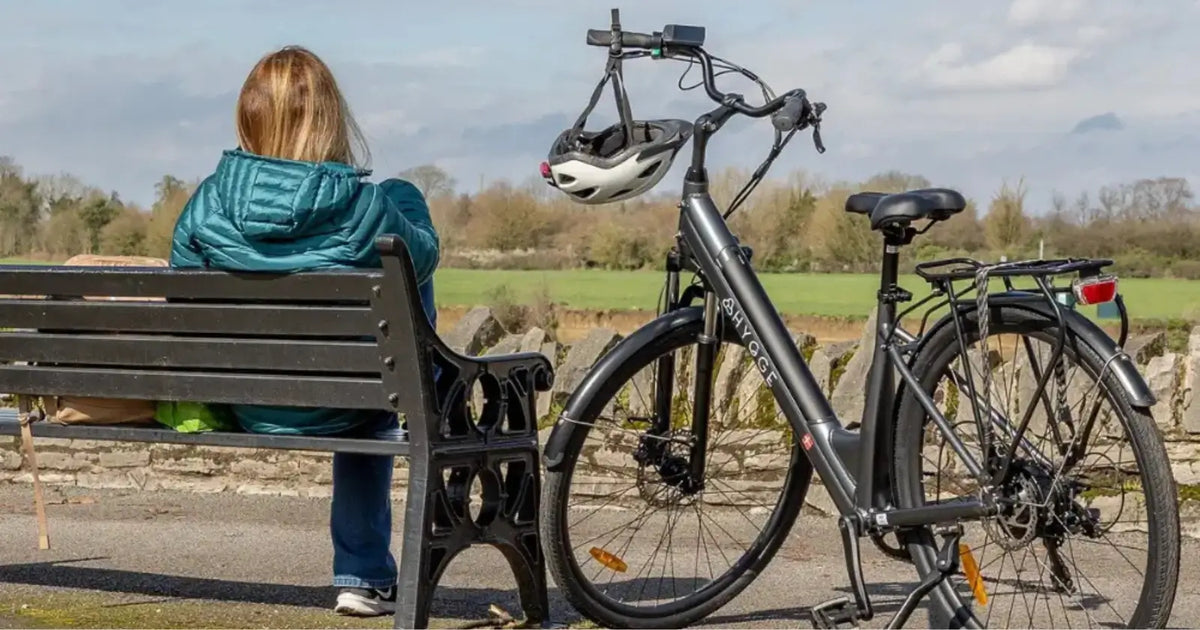 Hygge Aarhus Step-through electric bike parked beside a bench with a cyclist relaxing in a countryside setting.