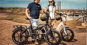 Couple standing with Hygge folding electric bikes near a coastal harbour on a sunny day.