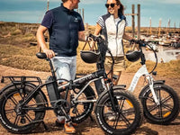 Couple standing with Hygge folding electric bikes near a coastal harbour on a sunny day.