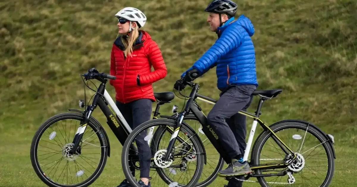Two cyclists riding Mark2 X-Cross electric bikes on a countryside path while wearing helmets and outdoor cycling gear.