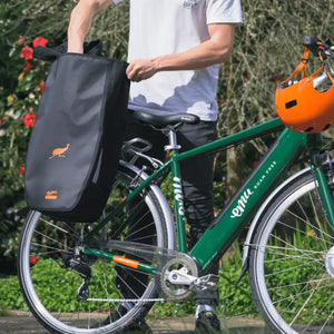 A pannier bag on the rear rack of a green Emu Roam electric bike, featuring commuter setup, rear rack storage, and urban cycling accessories.