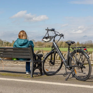 Step through electric bike with rider sat on a bench on a sunny sping day.