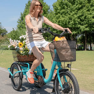 Woman cycling the Aitour Heal Mini folding electric trike loaded with flowers and groceries in the baskets.