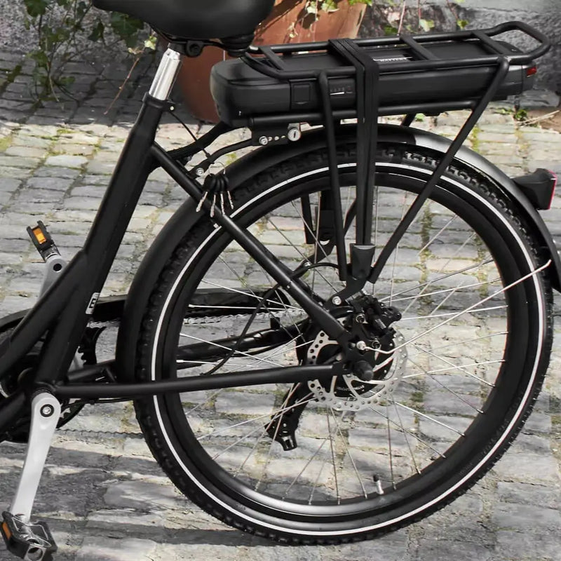 Close-up of the rear wheel, disc brake, and battery rack integrated into the frame of an Amcargobikes Ultimate Curve electric cargo bike parked on a cobblestone street.