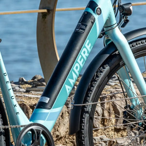 Blue Ampere Deluxe step-through hybrid electric bike 250W with integrated battery, parked near a coastal railing.