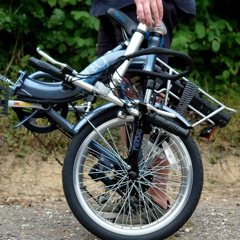 Folded Basis Osprey Low Step Folding Electric Bike 250W being carried by a person, showcasing its portability and compact design.