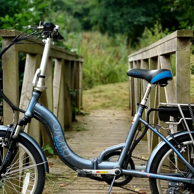 Basis Osprey Low Step Folding Electric Bike 250W parked on a wooden bridge in a scenic outdoor setting