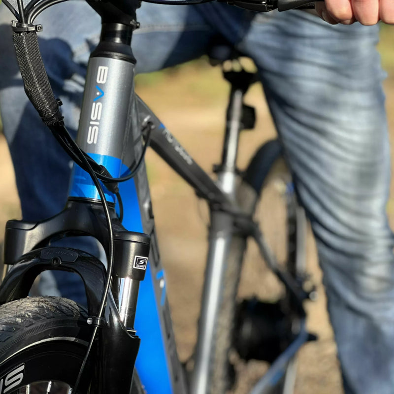 Front view of the Basis Protocol electric bike showing the suspension fork, head tube with logo, and a rider in motion.