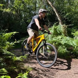 Rider in a helmet riding a yellow Batribike Delta LTD electric mountain bike on a woodland trail