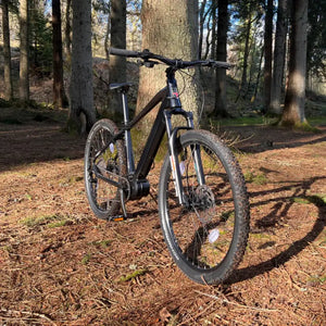 Batribike Delta Plus electric hardtail mountain bike parked in a forest setting, highlighting knobbly tyres for trail riding.