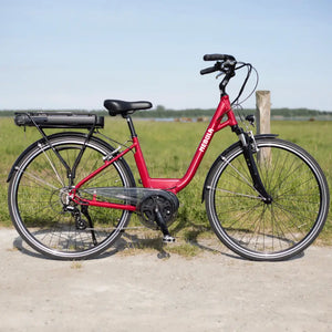 Side view of the Batribike Nebula Classic electric bike in red with a step-through frame, photographed outdoors on a gravel path.