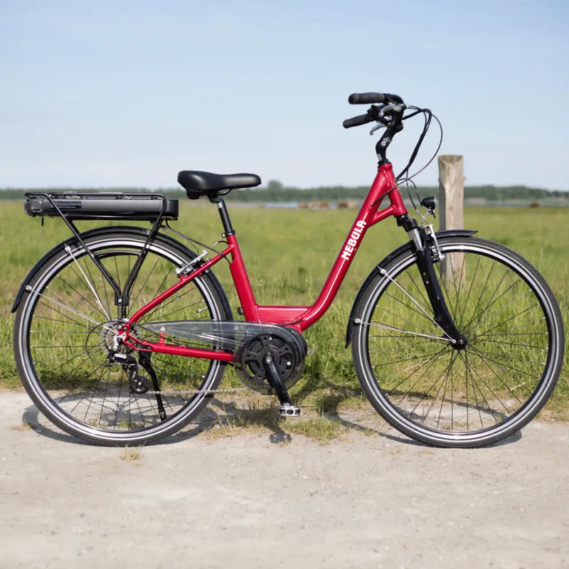 Side view of the Batribike Nebula Classic electric bike in red with a step-through frame, photographed outdoors on a gravel path.