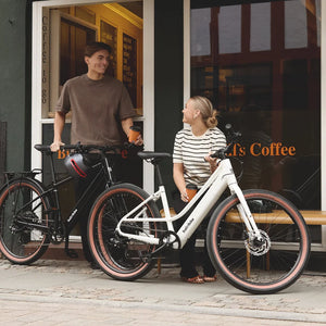 Man and woman standing with a black Batribike Route X and a white Route S outside a coffee shop