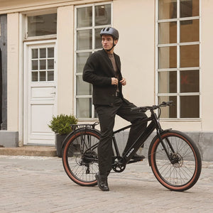 Man in a helmet standing astride a black Batribike Route X electric bike on a cobbled street