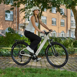 Woman wearing a helmet riding a cream Batribike SUV S electric bike along a cobbled urban path.