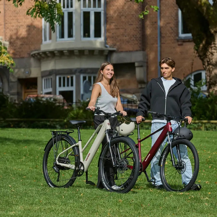 Two people standing on grass with Batribike electric bikes in cream and red.