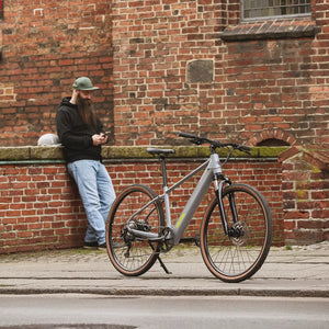 Man leaning on a brick wall checking his phone next to a parked grey Batribike Tour X