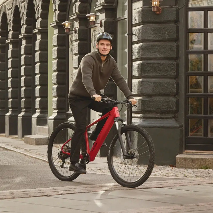 Man wearing a helmet riding a red Batribike Trail electric mountain bike along a cobbled city street.