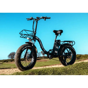 Big Game Bikes Impala folding fat tyre electric bike parked on a grassy trail under a clear blue sky.