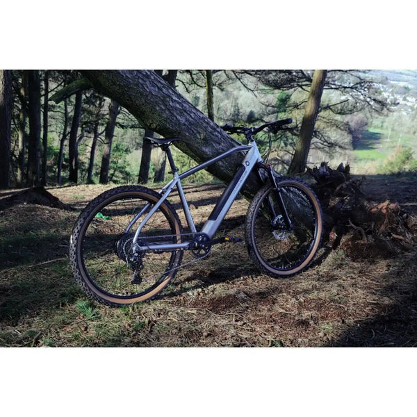 Rear view of the Claud Butler Ridge 2.0 Electric Mountain Bike (2025) on a forest trail, displaying the full drivetrain, wide tyres, and upright geometry