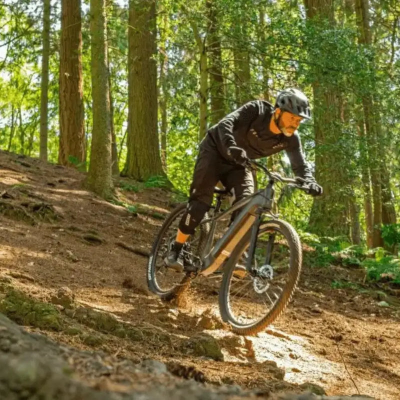 Rider navigating a forest trail on the Claud Butler Wrath 1.0 Cues electric mountain bike, built for off-road performance with 250W motor and robust tyres.