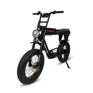 Front angled view of the Cruz73 electric off-road bike in black with thick tread tyres, front suspension, and LED headlight.