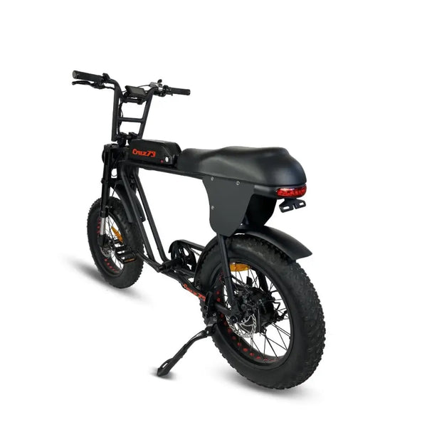 Rear left view of the Cruz73 electric off-road bike in black, showing the long padded seat, rear LED light, and fat tyres for rugged terrain.