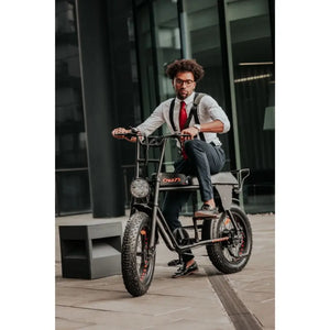 Man riding the Cruz73 Retro Fat Tyre Electric Bike in a modern urban setting, wearing formal attire and a red tie for a stylish commuter look.